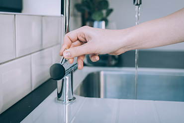 A horizontal shot of a human hand opening the modern sink for the flow of water